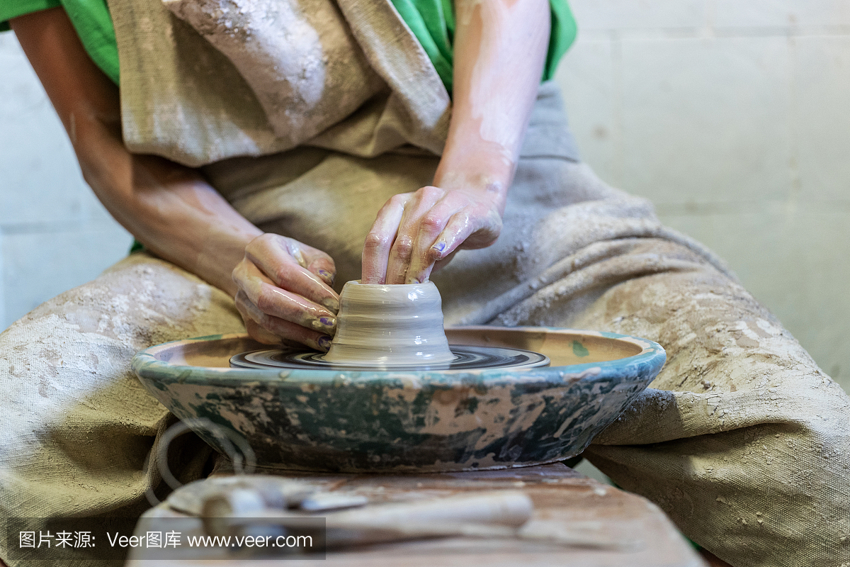 近近裁剪照片的女士在她的工作,她坐在工作空间内生产陶土产品的双手享受过程